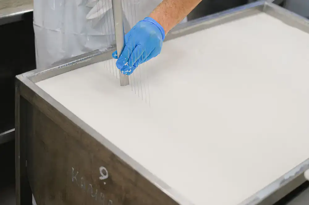 Overhead view of a person cutting fresh curds in a vat